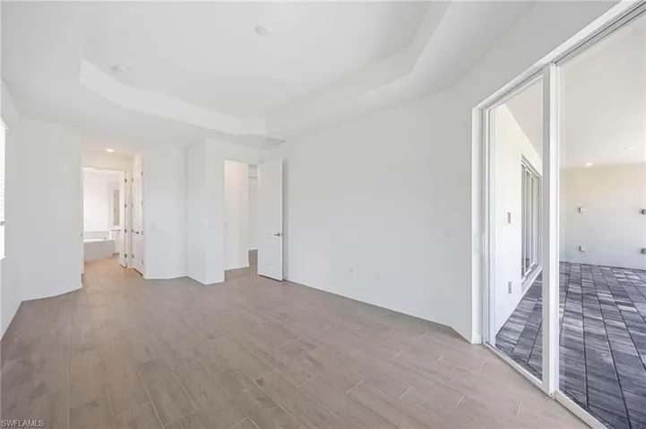 Unfurnished bedroom with baseboards, connected bathroom, light wood-style flooring, and a tray ceiling