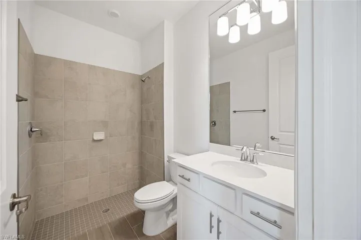 Full bath featuring toilet, tiled shower, and vanity
