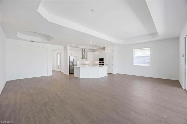 Unfurnished living room featuring a sink, baseboards, a tray ceiling, and wood finished floors