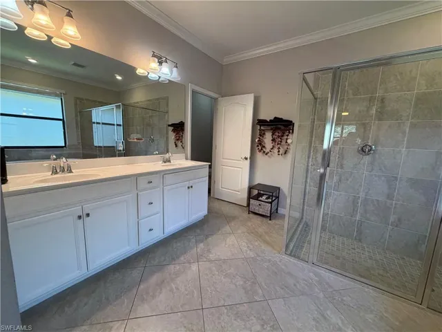 Master bath with double vanity, crown molding, and a shower stall