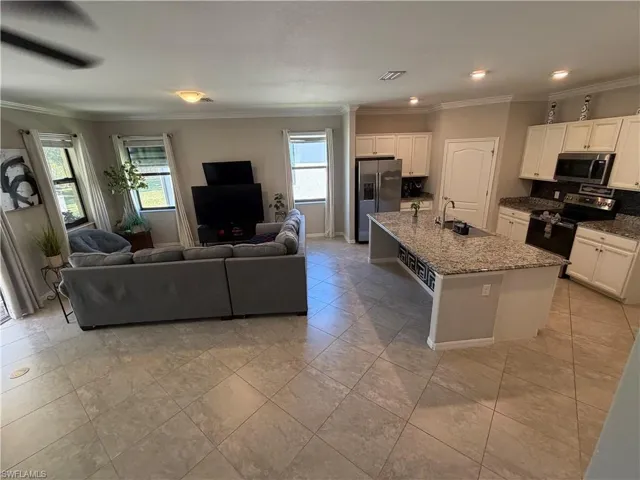 Kitchen featuring stainless steel appliances, white cabinetry, dark stone counters, ornamental molding, and open floor plan