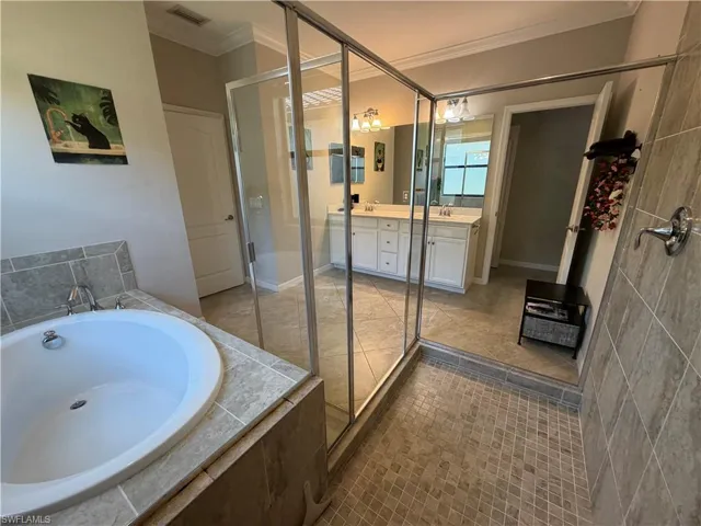 Master bath featuring ornamental molding, a garden tub, vanity, a shower stall, and dark tile patterned flooring