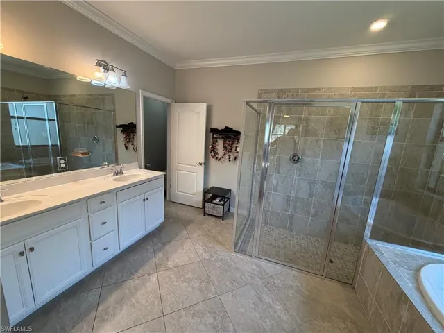 Bathroom featuring double vanity, crown molding, a stall shower, a relaxing tiled tub, and light tile patterned floors