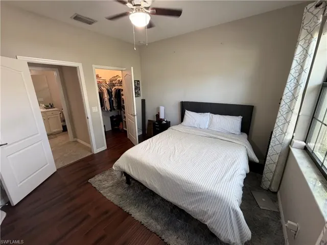 Bedroom with dark wood finished floors, a spacious closet, and a ceiling fan