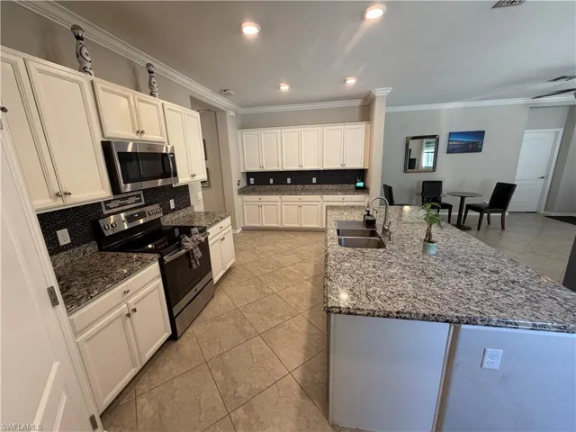 Kitchen featuring stainless steel appliances, light tile patterned floors, white cabinets, dark stone countertops, and tasteful backsplash