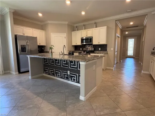 Kitchen with stainless steel appliances, white cabinetry, dark stone counters, ornamental molding, and a kitchen island with sink