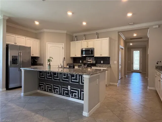 Kitchen with white cabinetry, stainless steel appliances, dark stone countertops, decorative backsplash, and ornamental molding
