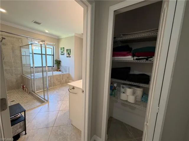 Bathroom featuring vanity, a stall shower, light tile patterned floors, a bath, and crown molding