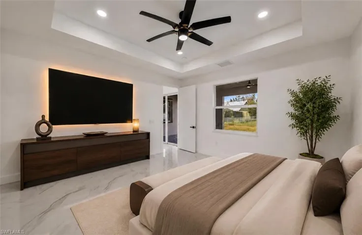 Recessed ceiling with integrated lighting, a ceiling fan, large window, and an entertainment console with backlighting