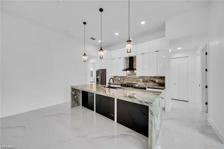 Kitchen featuring a waterfall island, sleek white cabinetry, pendant lighting, built-in range hood, and large format tile flooring