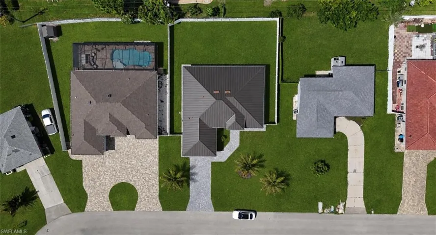 Paver driveway, mature palm trees, manicured lawn, and screened pool enclosure