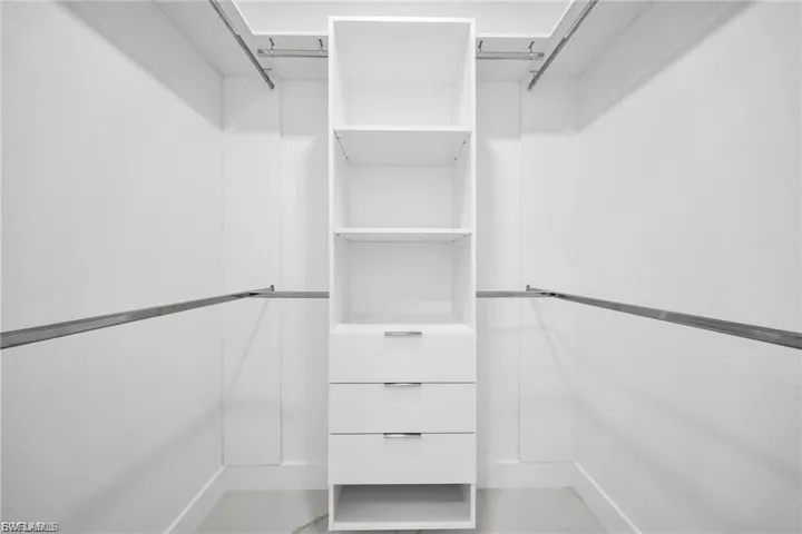 Custom closet system featuring white shelving, multiple hanging rods, and integrated drawers with polished chrome hardware