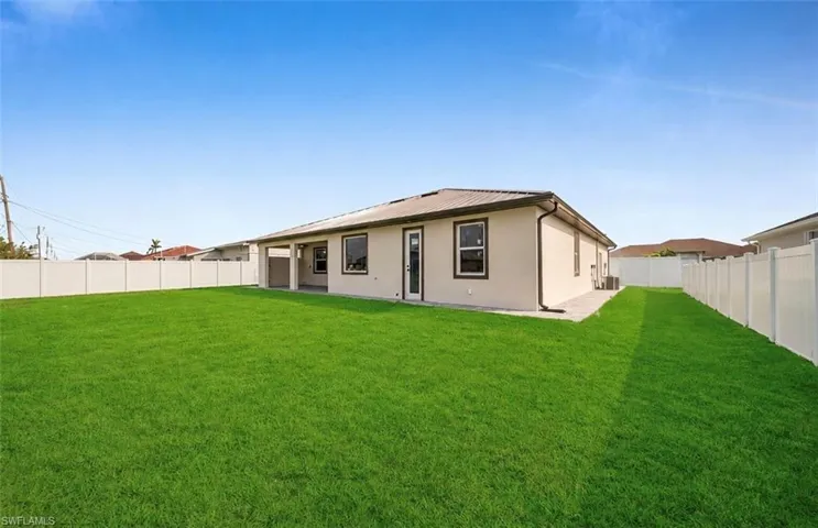 Expansive grassy backyard featuring a full privacy fence, covered patio, and stucco exterior