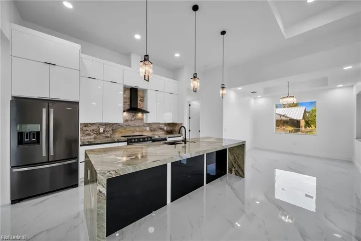 Gourmet kitchen featuring a large waterfall island, integrated cooktop, stainless steel refrigerator, and pendant lighting