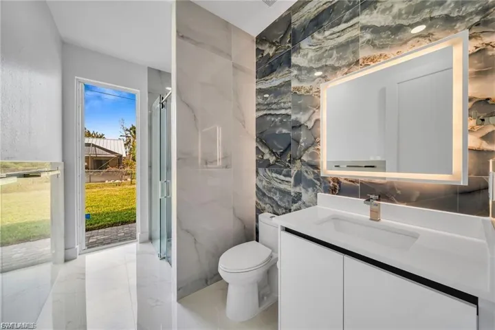 White floating vanity with integrated sink, gold-finish faucet, and an illuminated mirror