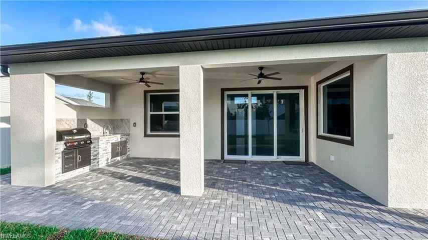 Expansive covered patio featuring an outdoor kitchen with built-in grill, sink, and stone-finish backsplash