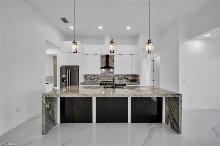 Waterfall island with integrated cooktop, white gloss cabinetry, marbled backsplash, and three pendant light fixtures