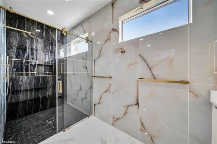 Frameless glass shower enclosure with brass-finish hardware, black marble-look shower walls, and white marble-look wall tiling