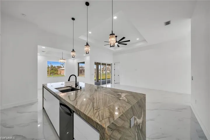 Kitchen island with waterfall countertop, integrated sink, and modern pendant lighting