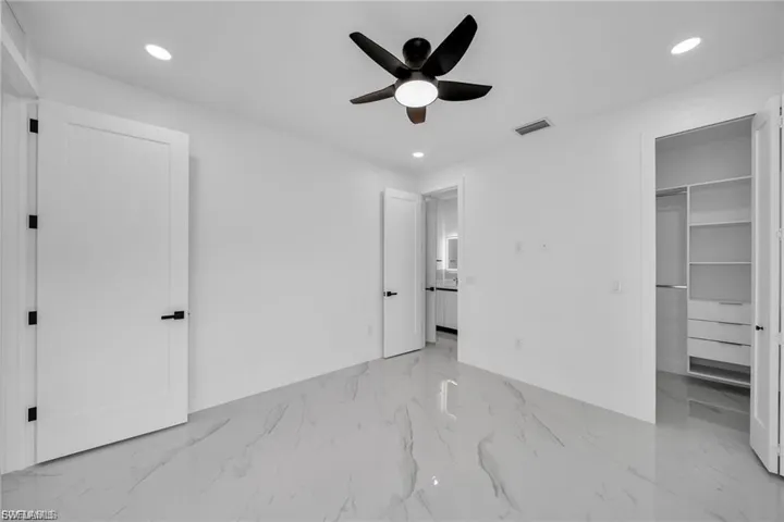 Spacious room featuring white walls, large format tile flooring, a ceiling fan with integrated lighting, recessed lighting, and a built-in closet system