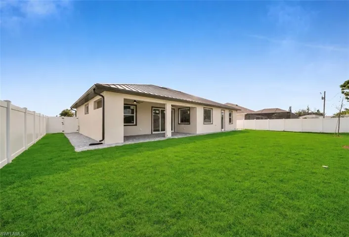 Spacious backyard featuring a manicured lawn, full privacy fencing, and an expansive concrete patio