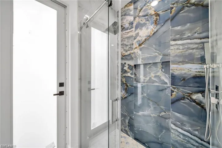Walk-in shower featuring a glass enclosure, patterned tile walls, built-in shower niche, and a fixed showerhead with a handheld sprayer