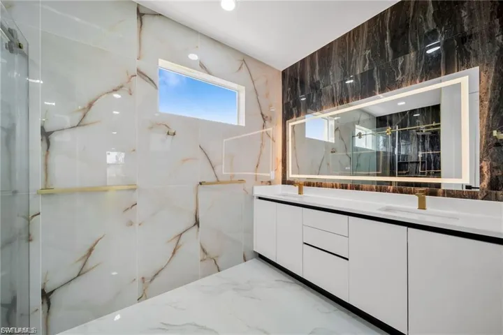 Dual vanity with white cabinetry and integrated sinks, illuminated mirror, and gold-finish fixtures