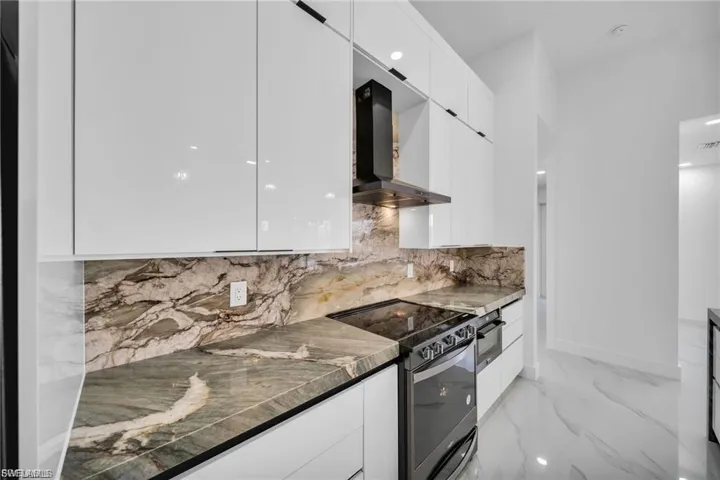 Sleek kitchen with white high-gloss cabinetry, stone countertops, and a matching stone backsplash