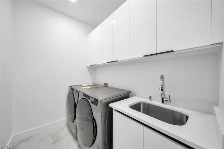 White upper cabinetry with minimalist hardware, white countertop with an integrated stainless steel sink, and light-toned flooring