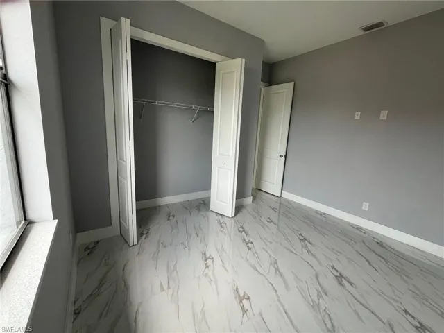 Unfurnished bedroom with marble finish floor, a closet, and baseboards