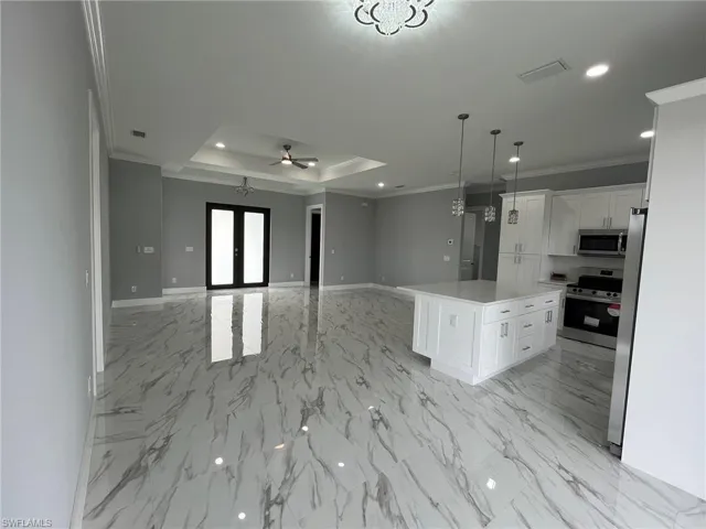 Kitchen featuring a tray ceiling, french doors, appliances with stainless steel finishes, ornamental molding, and white cabinetry