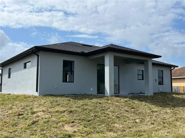 Rear view of property featuring stucco siding, roof with shingles, and a yard