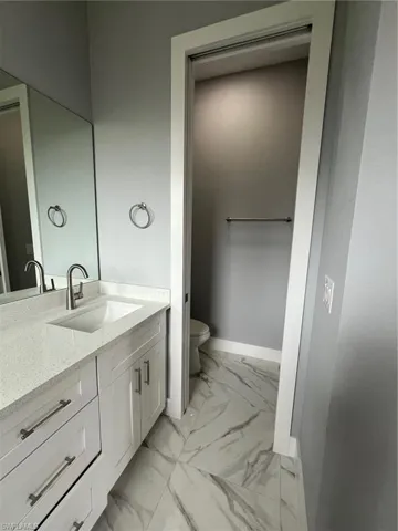 Bathroom with toilet, marble finish floor, baseboards, and vanity
