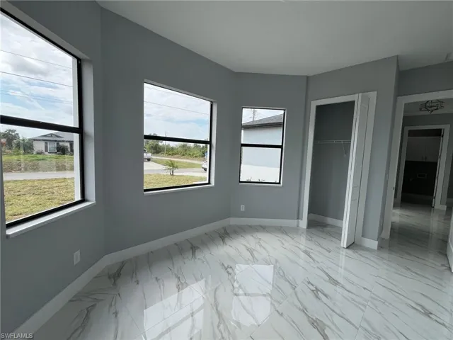 Unfurnished bedroom with marble finish floor, multiple windows, baseboards, and a closet