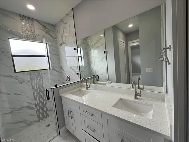 Bathroom featuring marble finish floor, a sink, a marble finish shower, and double vanity