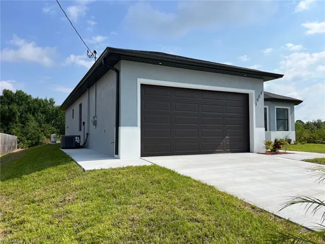 View of side of home with cooling unit, stucco siding, a lawn, an attached garage, and concrete driveway
