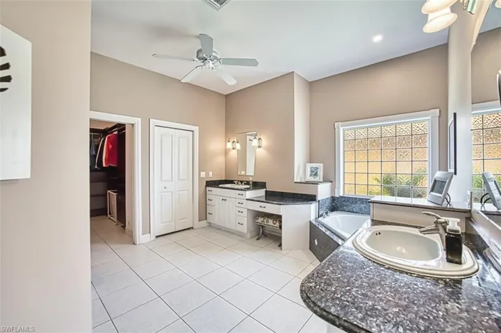 Primary bathroom with tiled flooring, vanity, a garden tub, and a ceiling fan, large walk in closet