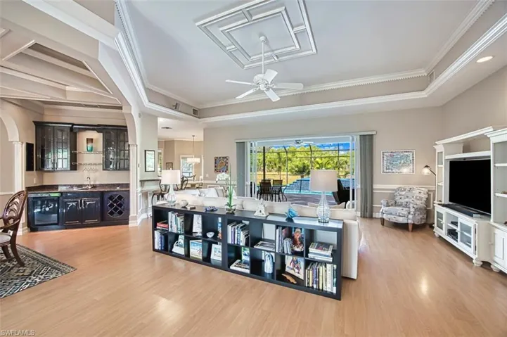 Living room featuring light wood-type flooring, a ceiling fan, crown molding, and a raised ceiling with sliding doors to pool area