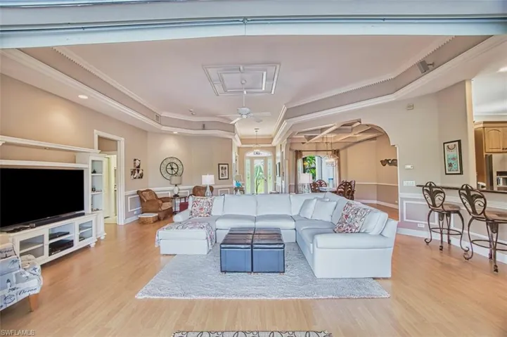 Living area featuring arched walkways, light wood-style flooring, crown molding, and ceiling fan