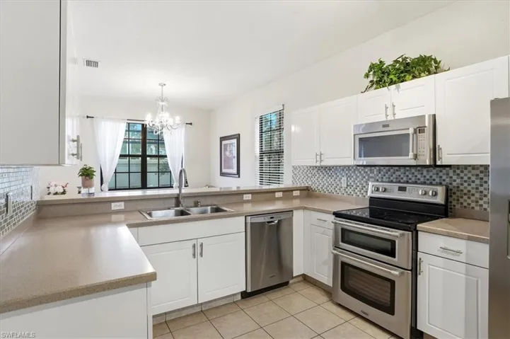 Kitchen with stainless steel appliances, white cabinets, decorative backsplash, hanging lights, and light tile patterned floors