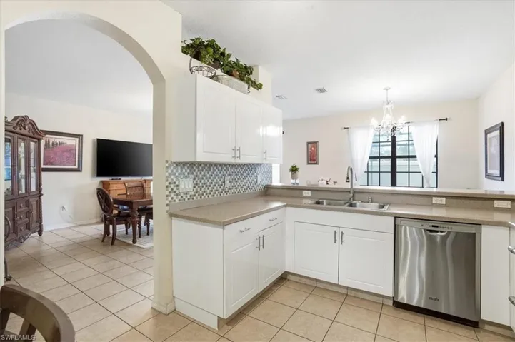 Kitchen featuring stainless steel dishwasher, white cabinets, light countertops, tasteful backsplash, and arched walkways