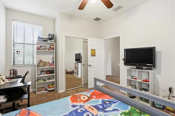 Bedroom featuring dark colored carpet, ceiling fan, a closet, and a desk