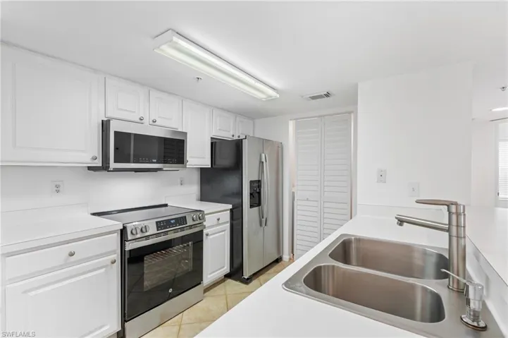 Kitchen with stainless steel appliances, white cabinetry, sink, and light tile patterned floors