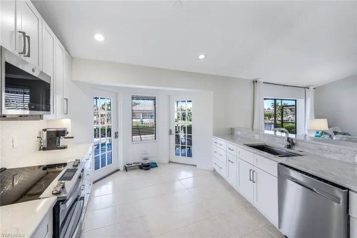 Kitchen with stainless steel appliances, backsplash, light tile floors, sink, and white cabinetry
