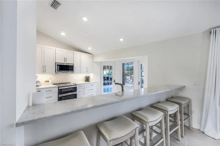 Kitchen featuring light stone countertops, tasteful backsplash, a breakfast bar, white cabinetry, and appliances with stainless steel finishes
