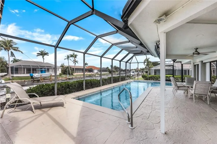 View of pool featuring glass enclosure, a patio area, and ceiling fan