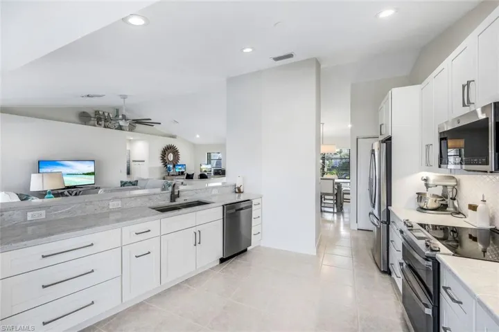 Kitchen with vaulted ceiling, light tile flooring, sink, white cabinets, and appliances with stainless steel finishes