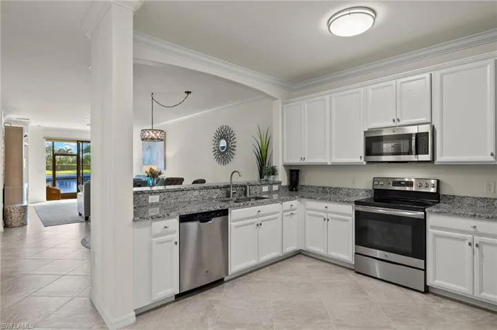 Spacious kitchen with crown molding, tile floors, white cabinetry, granite counters, stainless steel appliances, and tranquil lake views.