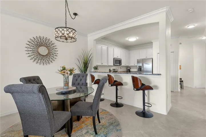 Fully furnished dining room with crown molding, ornamental chandelier, and tile floors.