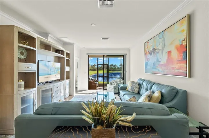 Fully furnished living room featuring an entertainment center, crown molding and tranquil lake views.